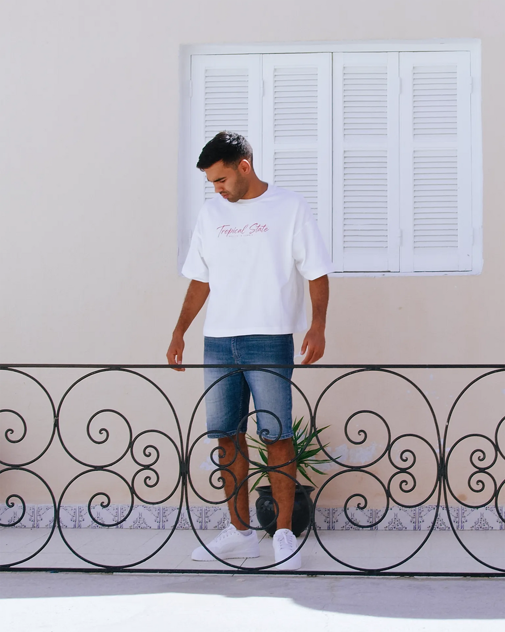Man wearing TROPICAL STATE™ white cropped oversized graphic T-shirt with dropped shoulders, denim shorts and White sneakers
